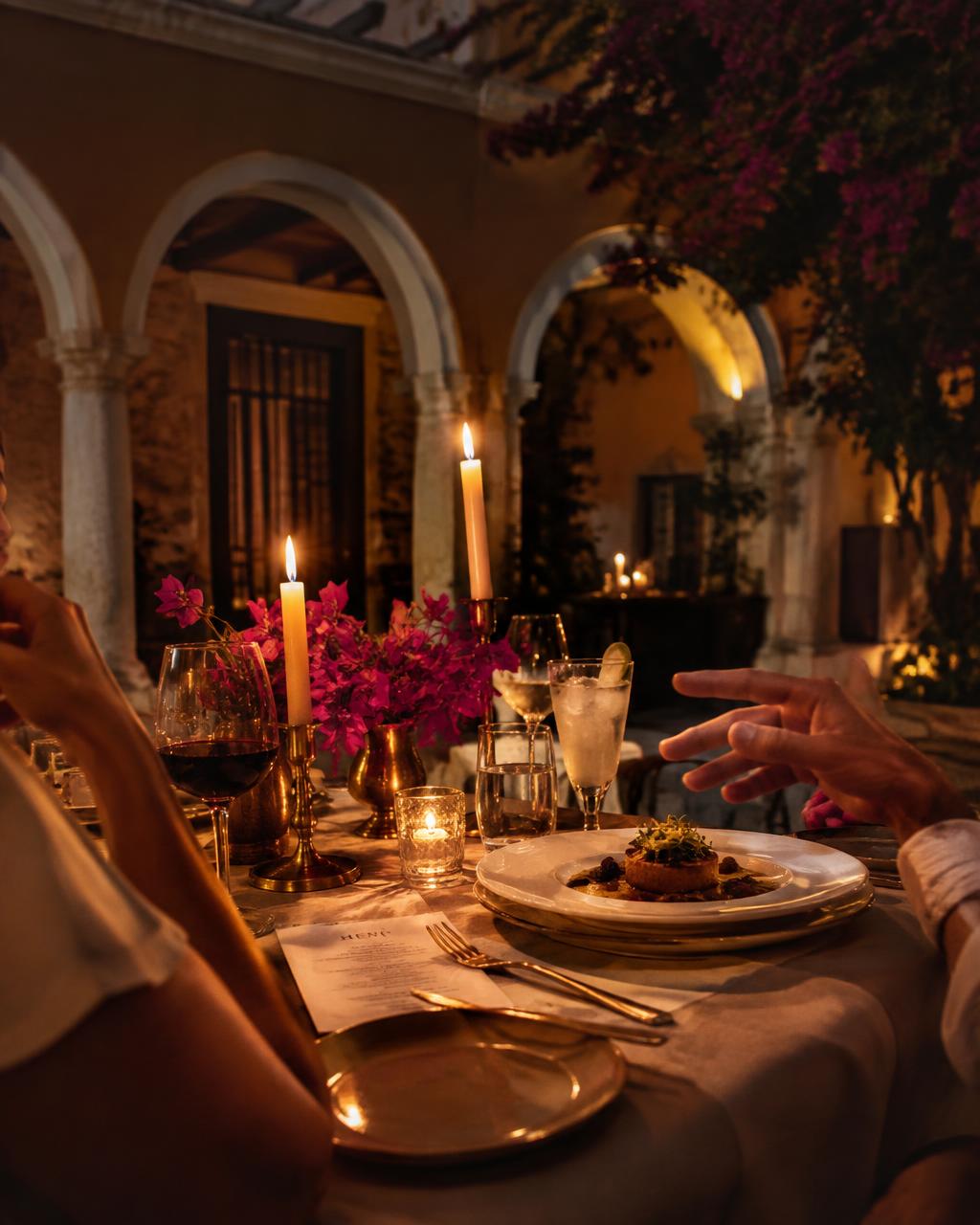 Candlelit supper table in a Mérida courtyard with guests reaching across
